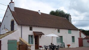 Un bâtiment blanc avec un toit recouvert de tuiles, une porte verte et une table entourée de chaises à l’extérieur.