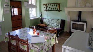 A dining area with a table set for two, a wooden chair, a hanging light fixture, and a television on a stand.