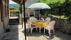 A patio with a table set for four, a grill, and a stone wall.