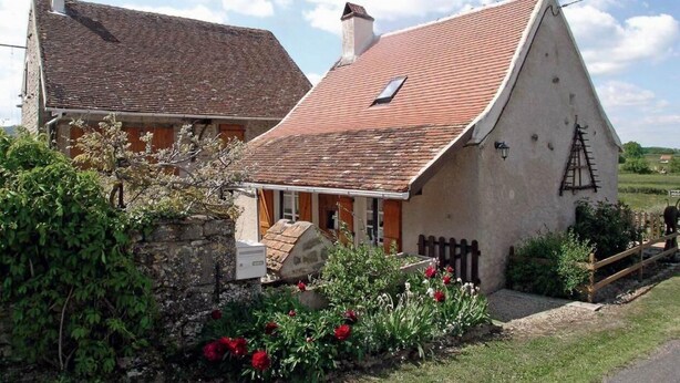 A traditional stone house with a sloped roof, a small porch, and a wooden fence.