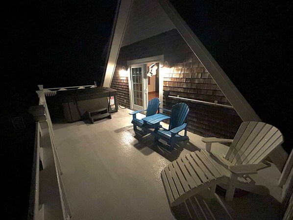 An outdoor deck with two chairs and a table, a covered area with a door, and a brick wall.