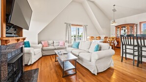 Amplio salón estilo loft con techo alto, chimenea, mesa de comedor y televisor montado en la pared.
