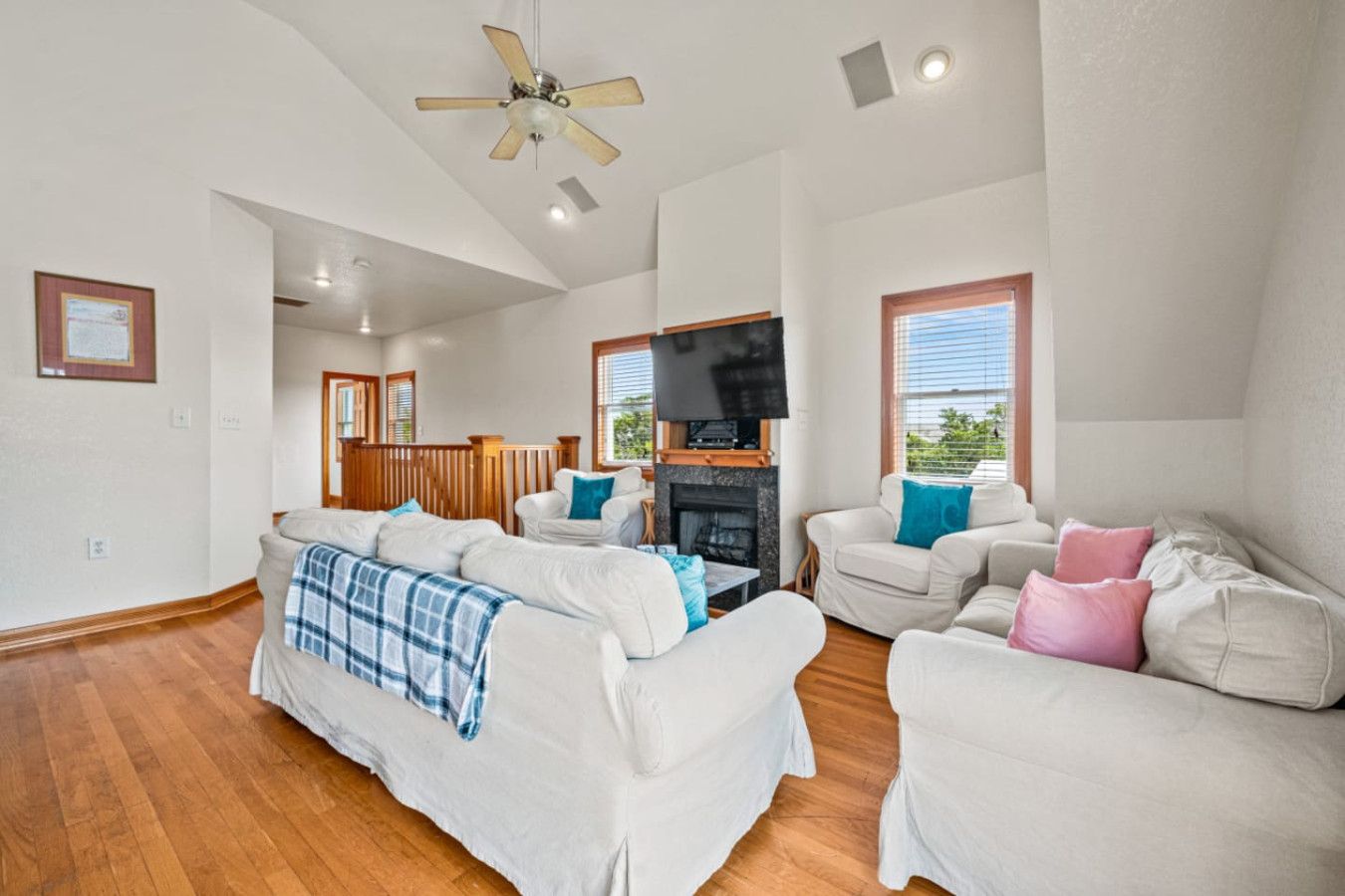 A spacious living room with a fireplace, a ceiling fan, and a television.