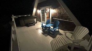 Un espacio de estar al aire libre cubierto con dos sillas Adirondack azules y una mesa, una parrilla y una puerta que da al interior.