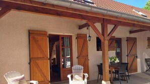 Een gebouw met een overdekte veranda, twee openslaande houten deuren, een kleine tafel met stoelen en een potplant.