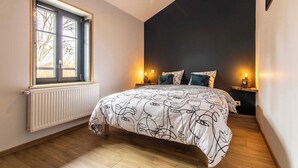 Ein Schlafzimmer mit großem Fenster, Heizkörper, Bett mit gemusterten Betttextilien und Nachttischlampen.