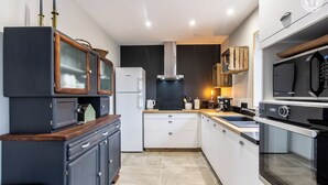 Eine kleine Küche mit dunklen Schränken, einem weißen Kühlschrank, einer Edelstahl-Dunstabzugshaube und einer Mikrowelle.