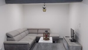Ein modernes Wohnzimmer mit einem grauen Ecksofa, einem kleinen Couchtisch, einer TV-Konsole und einer Deckenleuchte.