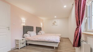 Ein Schlafzimmer mit Bett, Nachttischen, einer Wandleuchte, einem Heizkörper und einem Fenster mit Vorhängen.