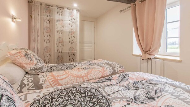 Ein Schlafzimmer mit einem Bett, gemustertem Bettwäsche, einem Fenster mit Vorhängen und einem Heizkörper.
