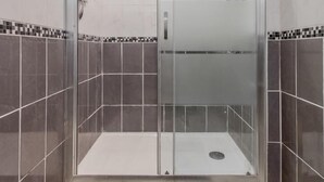 Eine moderne Duschkabine mit Glastür, gefliesten Wänden und einem dunklen Teppichboden.