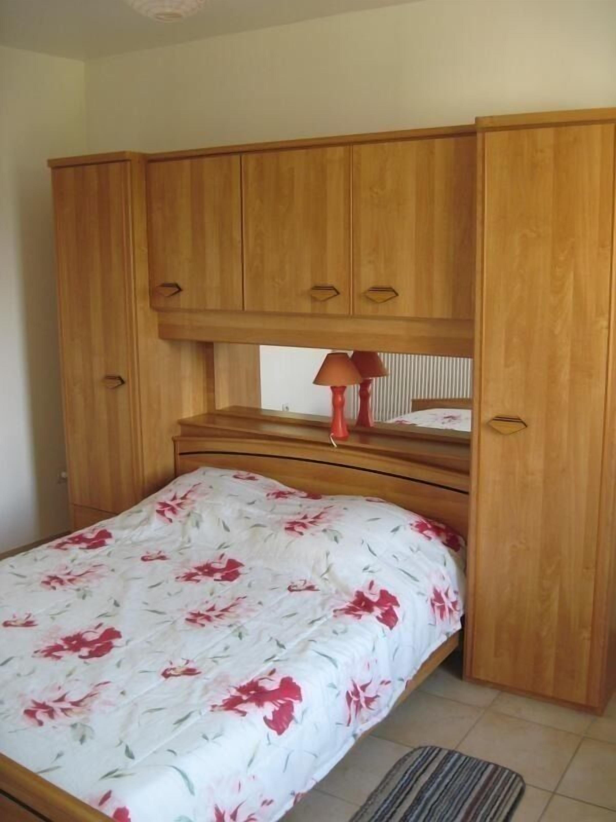 A bedroom with a bed, wooden wardrobe, and a nightstand with a lamp.