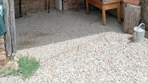 A rustic outdoor kitchen area with a stone wall, a wood-burning stove, a wooden table, and a metal bucket.