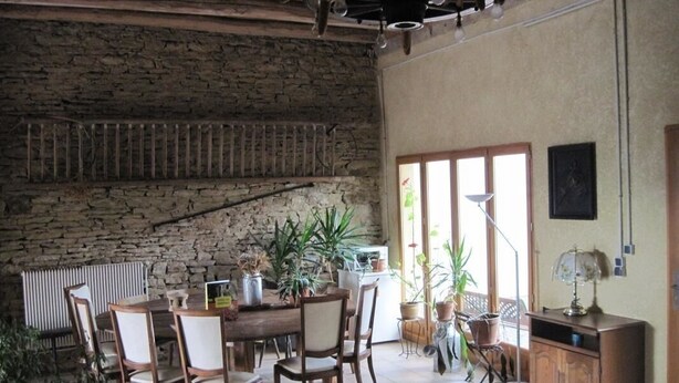 A rustic dining area with a stone wall, wooden table, chairs, and potted plants.