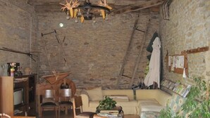 A rustic attic room with exposed stone walls, a wooden ceiling, a chandelier, a sofa, a coffee table, and a television.