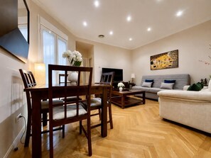 A living room with a sofa, a dining table with chairs, a TV, and a painting on the wall. - Gran Vía VI - Right in the Heart of Madrid (Madrid)