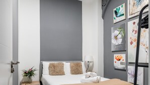A modern hotel room with a bed, a bedside table with a lamp, and a wall decorated with floral artwork.