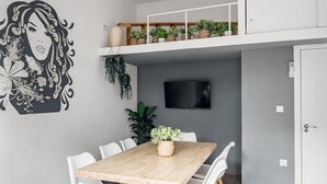 A modern dining area with a wooden table and white chairs, a mounted TV, and a wall with a decorative mural.