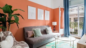 A modern living room with a grey sofa, a round glass coffee table, and a large potted plant.
