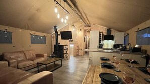 Un vaste espace de vie comprenant un coin repas avec une table en bois dressée pour le repas, un canapé en cuir et un coin cuisine équipé d’un four à micro-ondes et d’un évier.