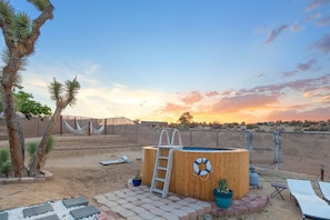 A backyard with a wooden hot tub, a ladder, lounge chairs, and a fenced area. - Alana House-Hot Tub, Pool, Fire Pit & Near Trails (Joshua Tree)