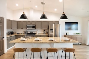 A modern kitchen with a central island, bar stools, and pendant lighting. - Alana House-Hot Tub, Pool, Fire Pit & Near Trails (Joshua Tree)