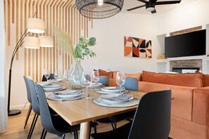 A dining area with a wooden table set for four, surrounded by chairs, a vase with greenery, and a modern pendant light.