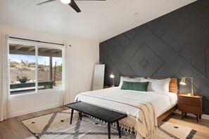 A bedroom with a bed, bedside tables, a bench, a window with curtains, and a view of the outdoors. - Alana House-Hot Tub, Pool, Fire Pit & Near Trails (Joshua Tree)