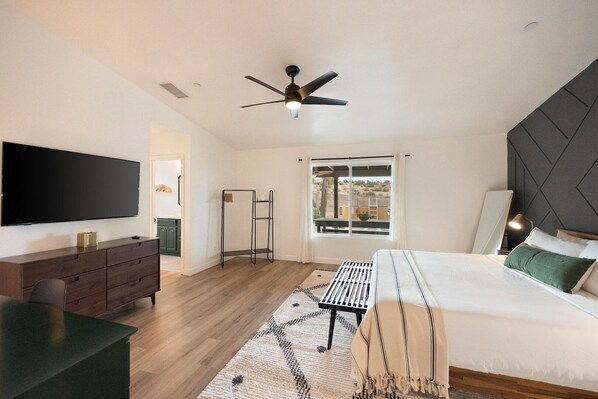 A modern bedroom with a bed, a TV, a desk, and a ceiling fan.