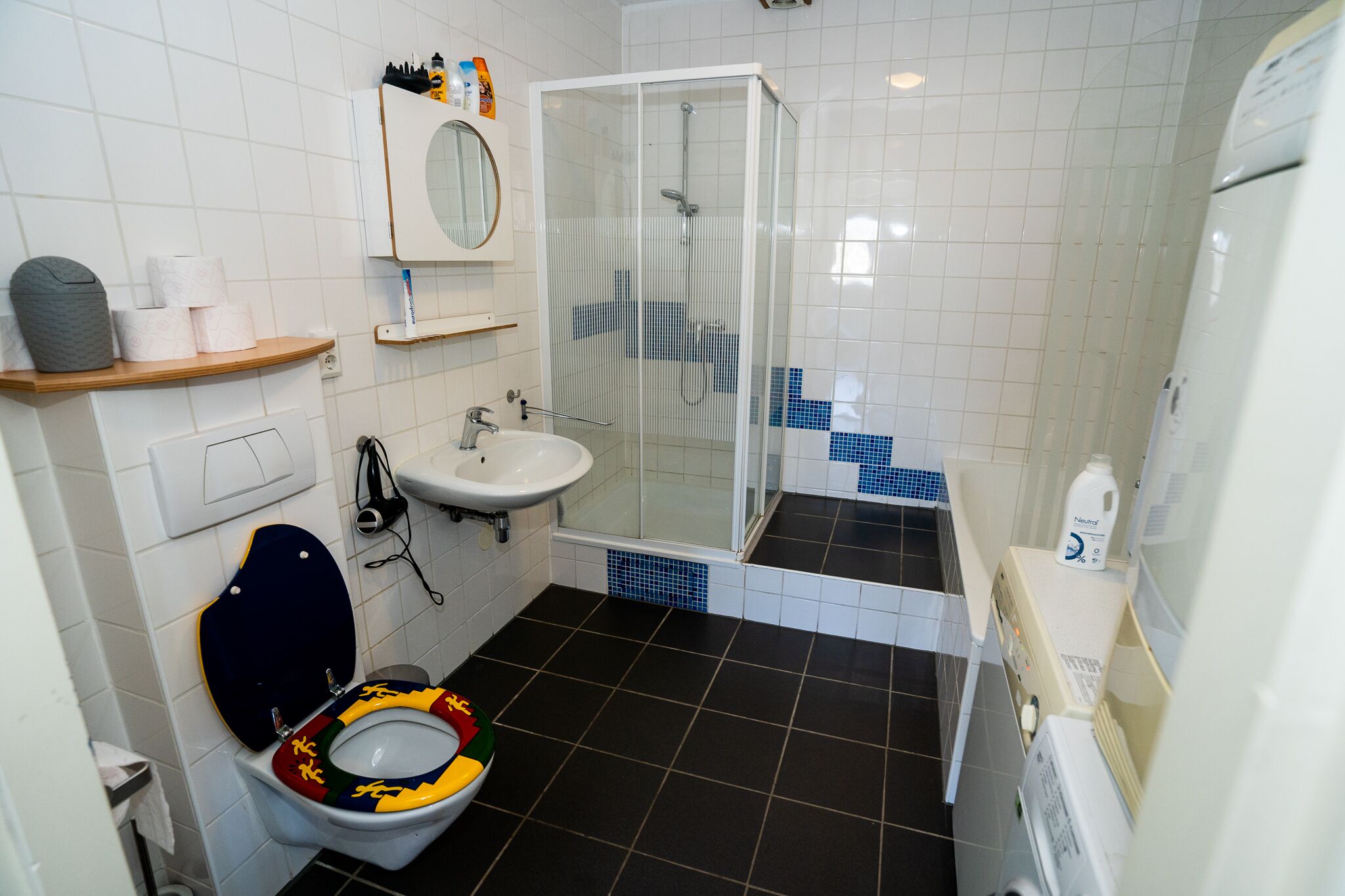 A bathroom with a toilet, sink, shower, and a mirror.