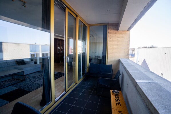 A modern apartment with a balcony, large sliding glass doors, a sofa, and a dining table.