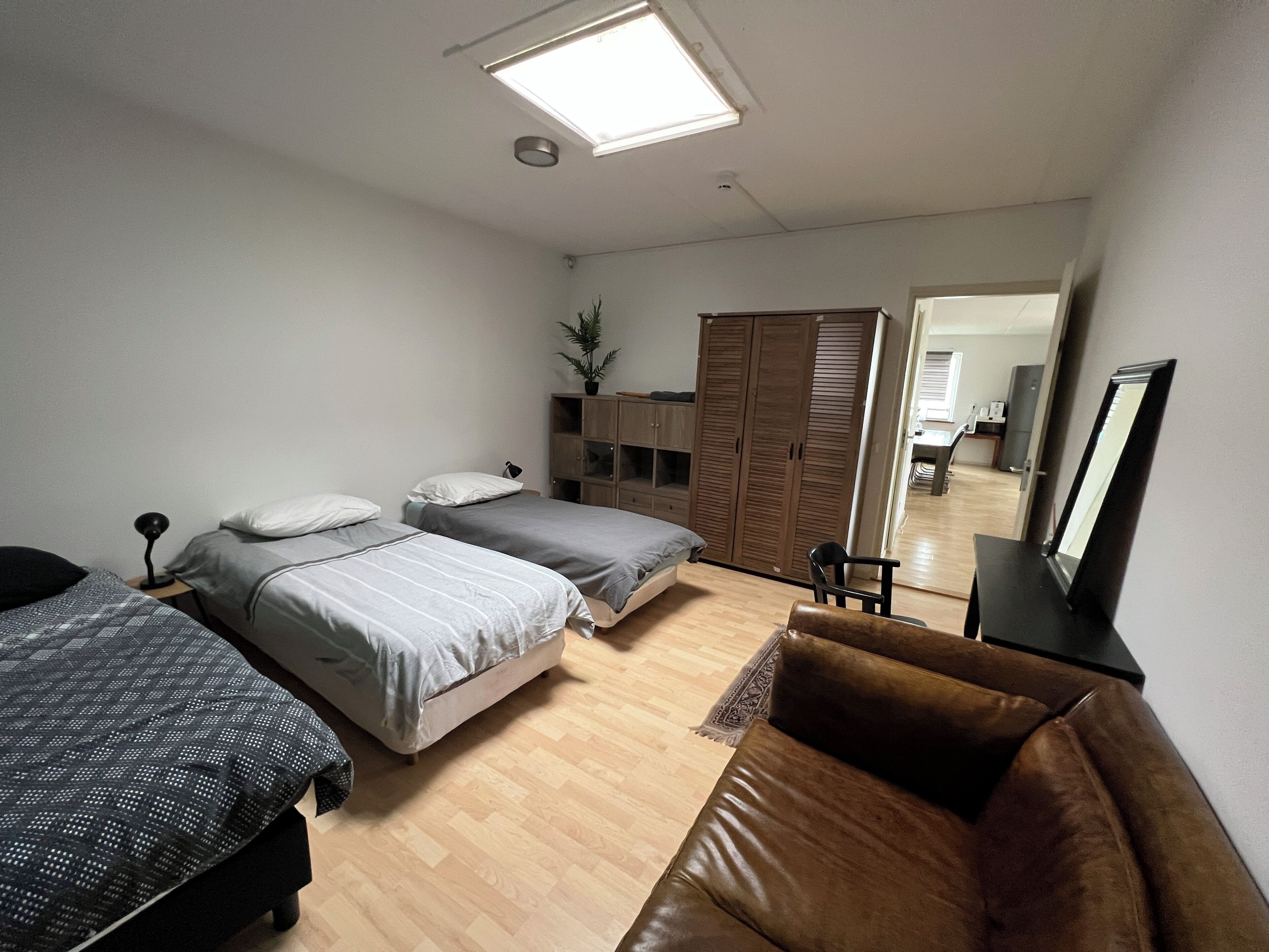 A bedroom with two beds, a brown leather sofa, a desk, and a wardrobe.