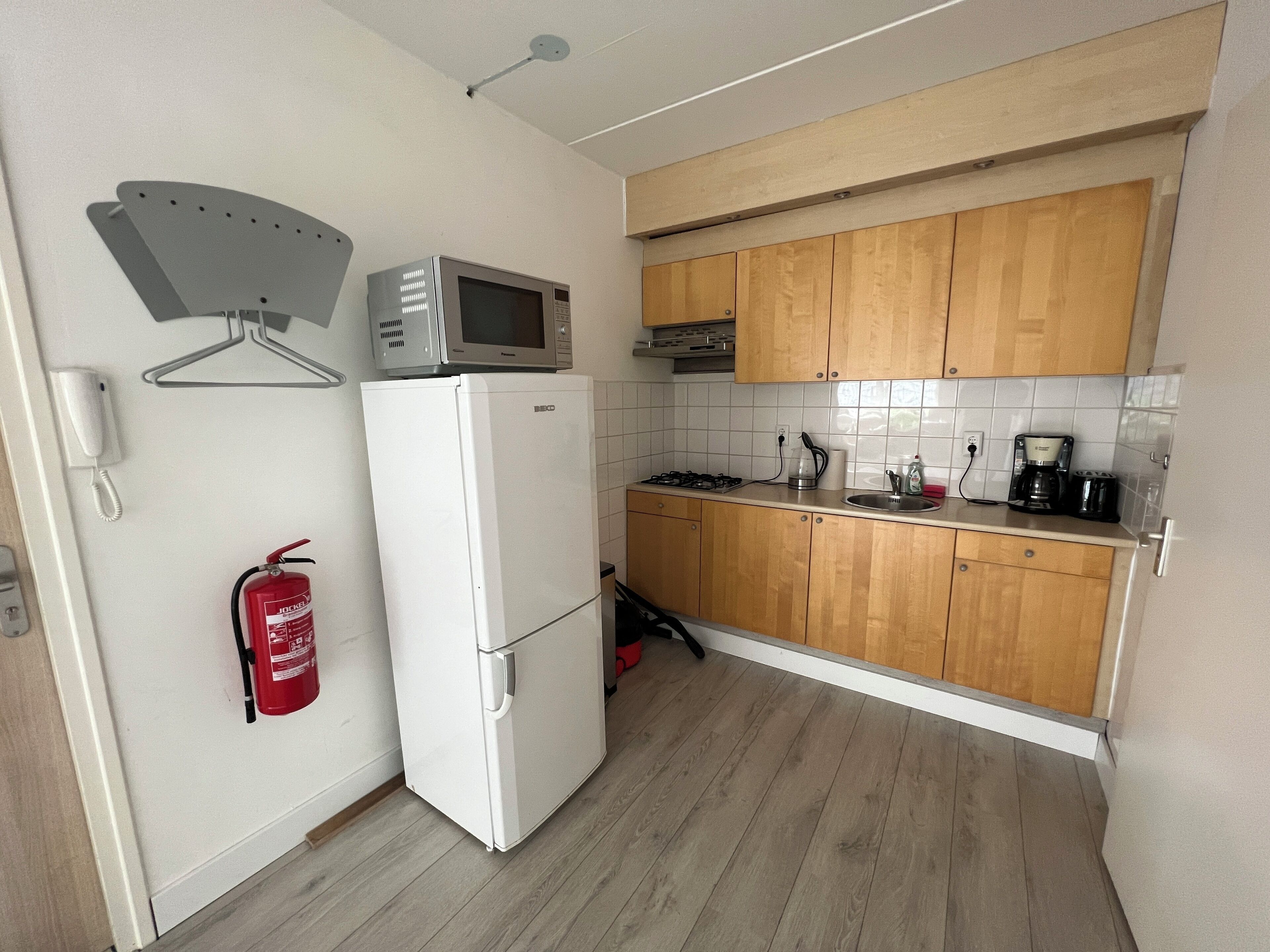 A compact kitchen with a white refrigerator, a microwave, wooden cabinets, a gas stove, and a coffee maker.