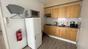 A compact kitchen with a white refrigerator, a microwave, wooden cabinets, a gas stove, and a coffee maker.