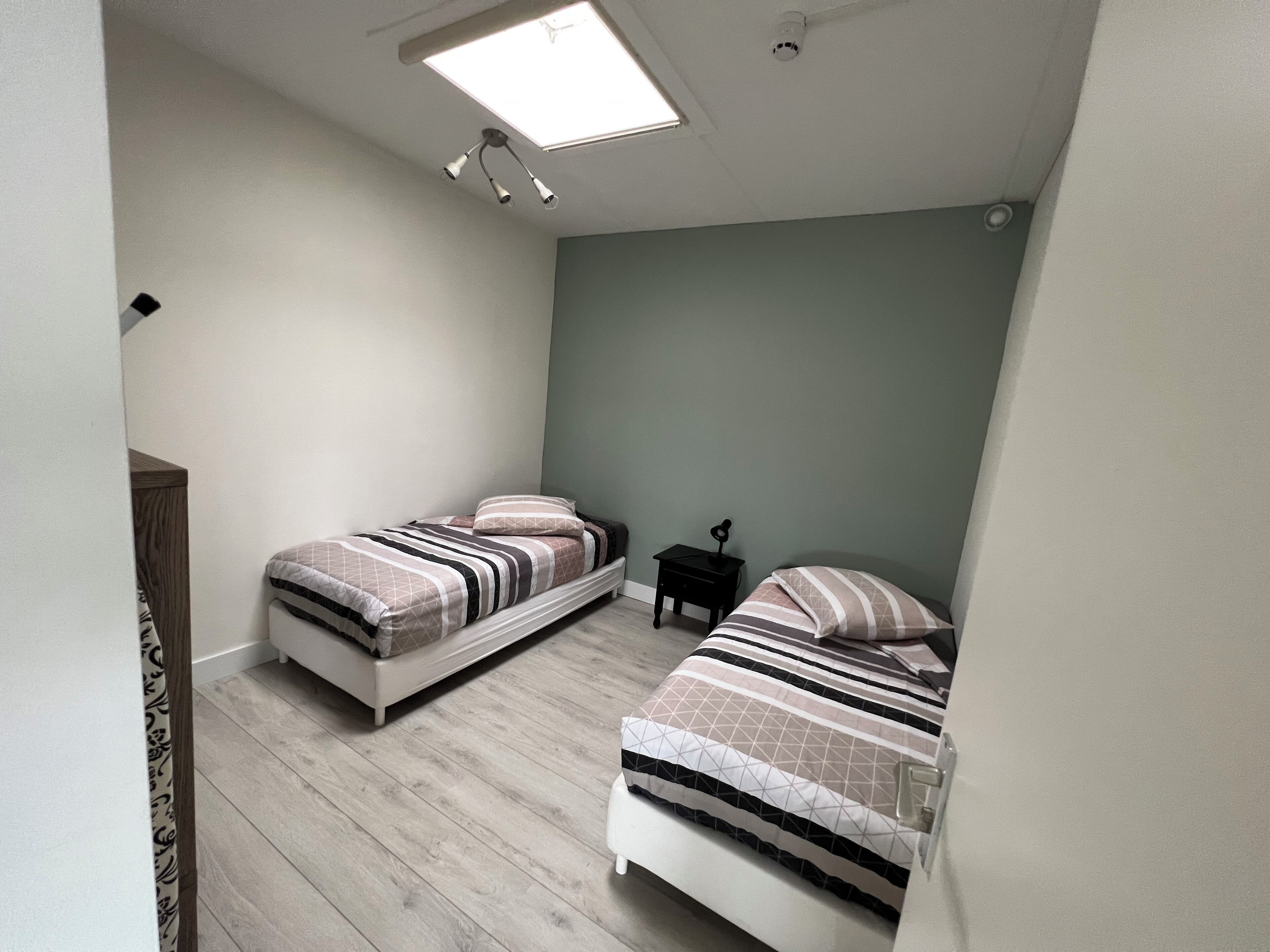 A small, narrow room with two beds, a nightstand, and a ceiling light.