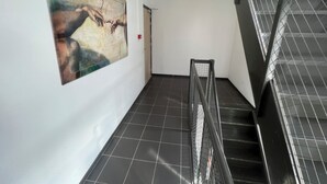 A corridor with a large abstract painting on the wall, a staircase with metal railings, and a tiled floor. - Zaanse Schans Apartments (Wormer)