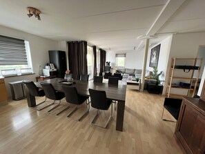 A modern living room with a dining area, large windows, and a flat-screen TV.