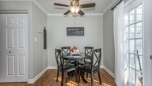 Un coin repas comprenant une table ronde, quatre chaises, un ventilateur de plafond et une fenêtre avec des rideaux.