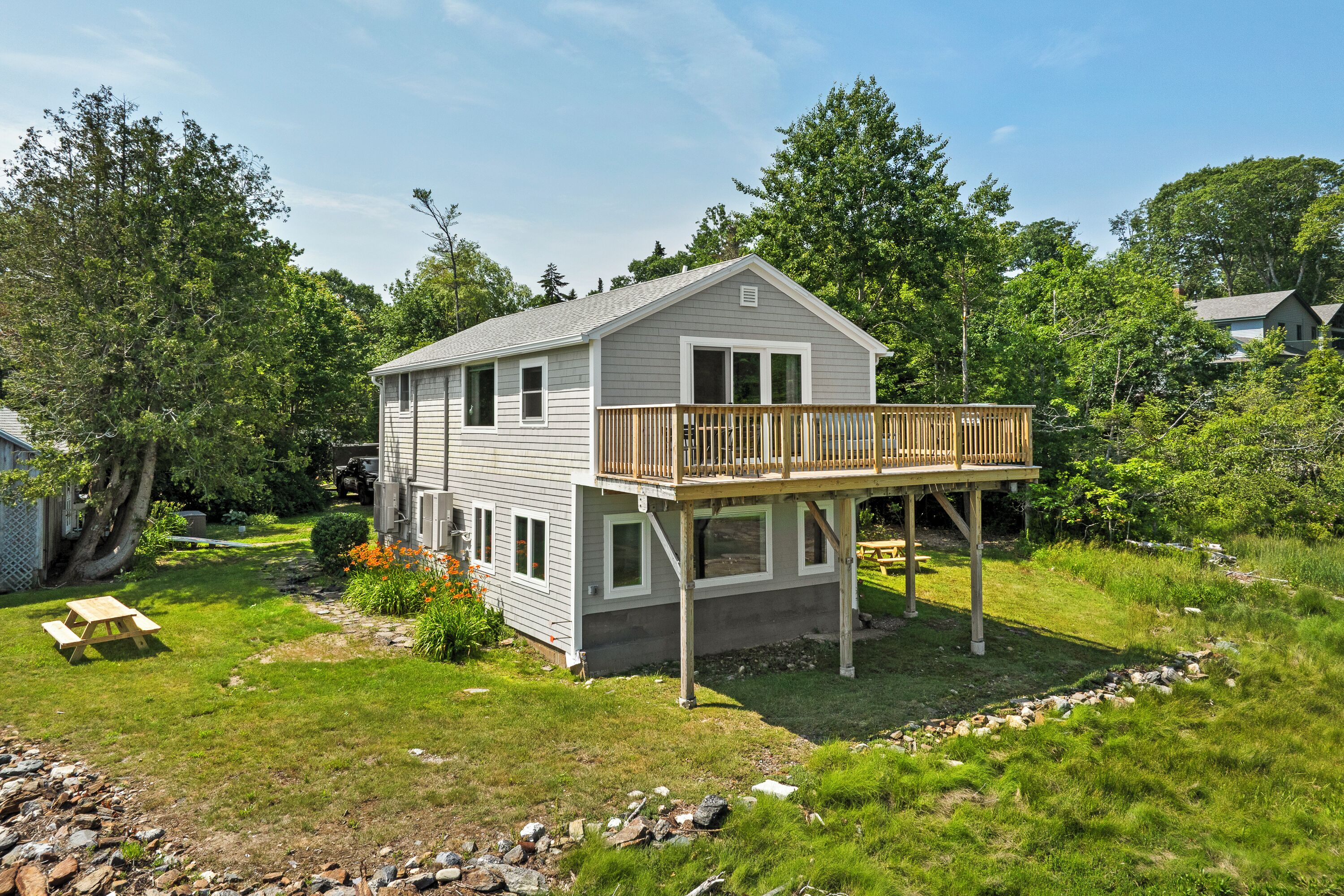 A two-story house with a deck, surrounded by a grassy yard and trees.