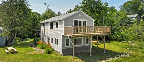 A two-story house with a deck, surrounded by a grassy yard and trees.