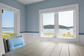 A room with a large window offering a view of a lake and boats, a wooden table, and a blue chair.