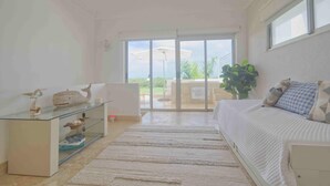 A spacious room with a glass door leading to an outdoor area, a bed with patterned pillows, a glass coffee table with decorative items, and a ceiling fan. - Stylish resort penthouse with amazing views (Punta Cana)