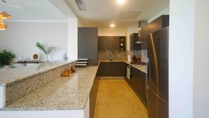A modern kitchen with granite countertops, dark cabinetry, and stainless steel appliances. - Stylish resort penthouse with amazing views (Punta Cana)