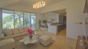 A spacious living area with a sofa, ottoman, and coffee table, a dining area with chairs and a table, and a kitchen with a counter and appliances. - Stylish resort penthouse with amazing views (Punta Cana)