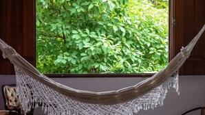 A hammock hanging in front of a window with a view of green foliage. - Pousada Arvoredo (Pirenópolis)