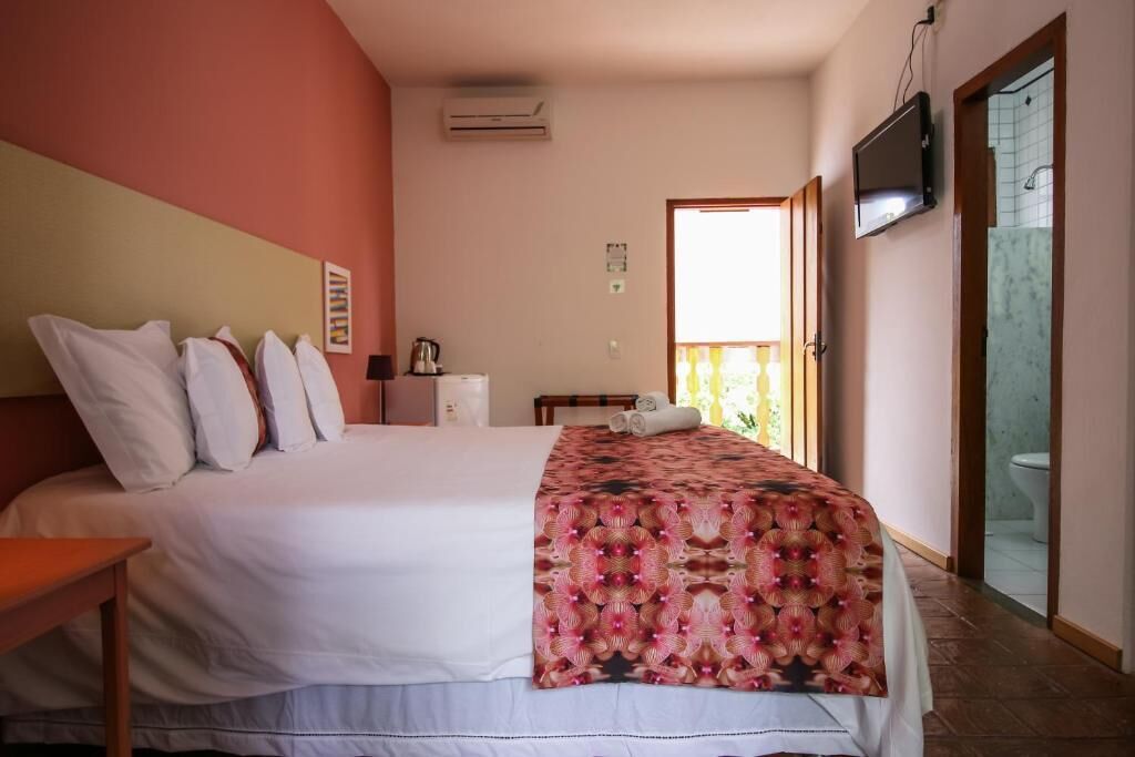 Une chambre d’hôtel avec un lit, une télévision, un climatiseur et une salle de bain visible à travers une porte ouverte.