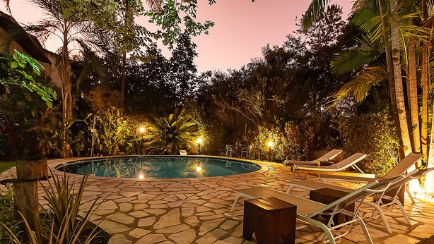 A circular pool with lounge chairs and a stone-tiled deck surrounded by tropical vegetation. - Pousada Arvoredo (Pirenópolis)