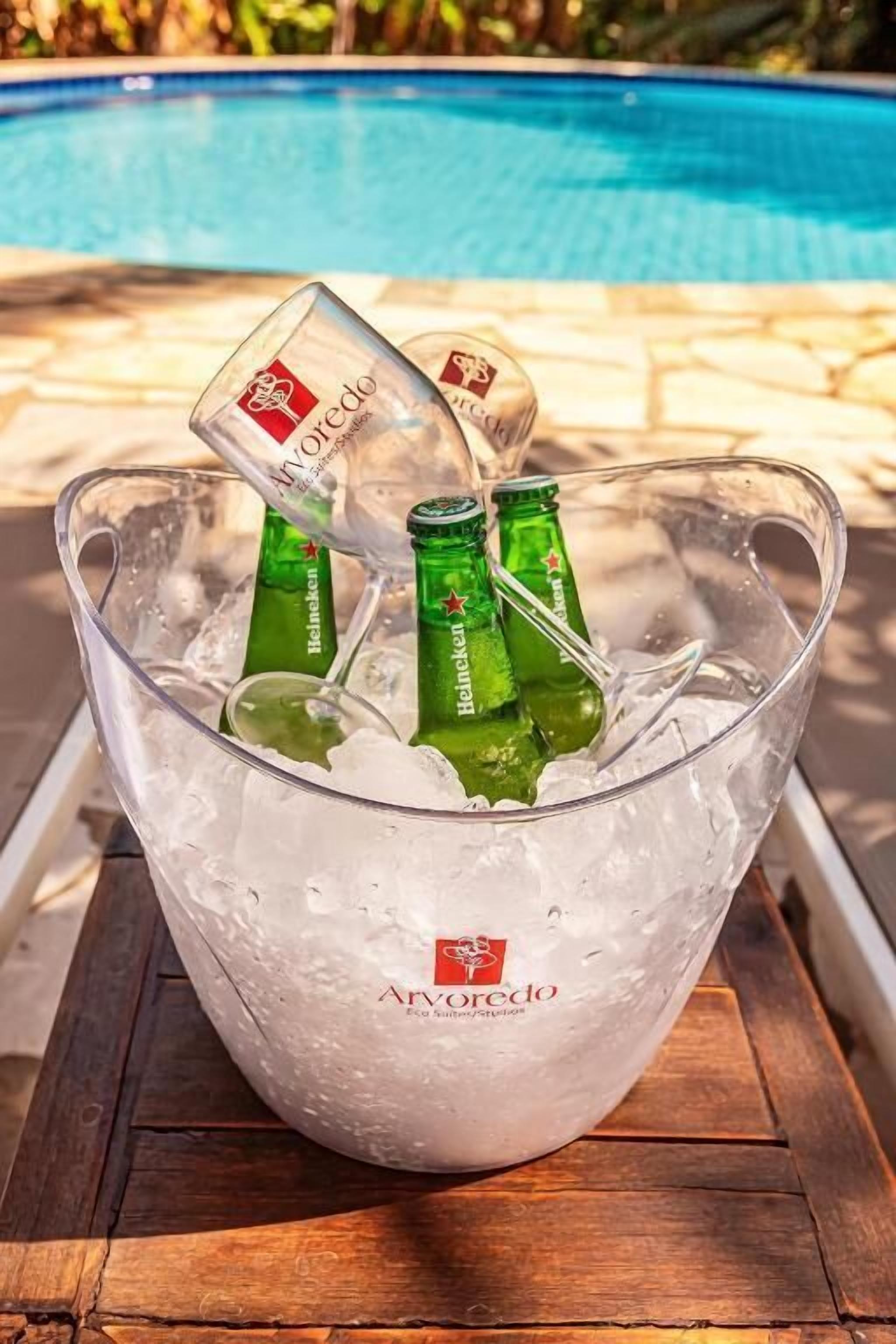 Un balde de vidrio transparente lleno de hielo y tres botellas de cerveza Heineken verdes.