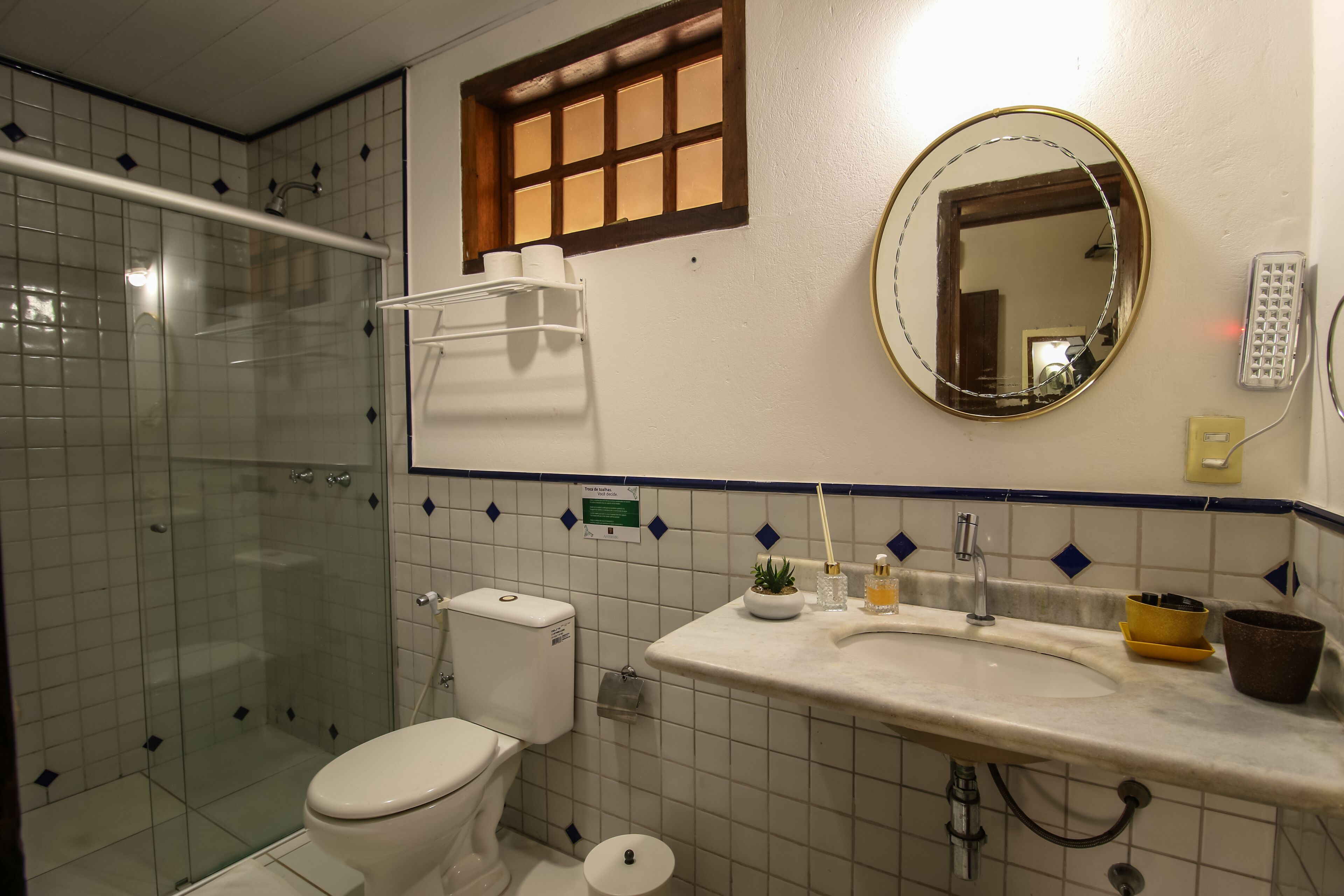 Un bagno con doccia vetro, un WC, un lavandino con specchio e una finestra sopra il lavandino.