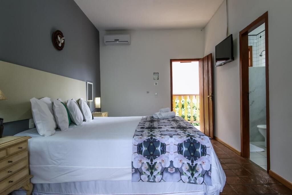 Un dormitorio con cama, mesita de noche, televisor y baño visible a través de una puerta abierta.